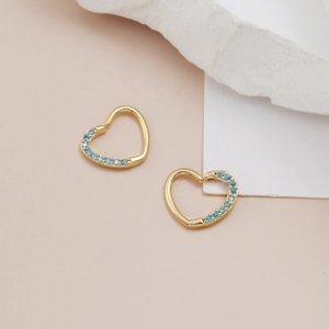 Detail of heart-shaped gold earrings with sky blue zircon inlay on white marble