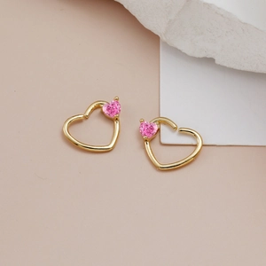 Dettaglio degli orecchini a cuore dorati con zircone rosa su sfondo beige chiaro