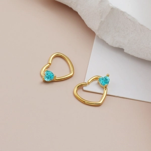 Dettaglio di orecchini a cuore in oro con pietre blu su sfondo moderno minimalista