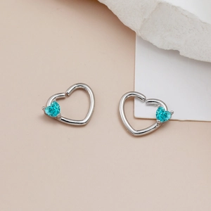 Dettaglio di piercing con gemme blu a forma di cuore su borchie in metallo argentato