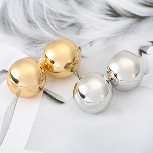 Orecchini a clip sferici lucidi in oro e argento su sfondo di piume decorative