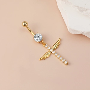 Gold navel ring with crystal cross and angel wings pendant on a stylish pink backdrop