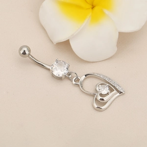 Detailed close-up of a silver heart-shaped navel ring with zircon inlay on a beige fabric