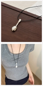 Detail of silver spoon pendant on black leather cord shown on wood and worn