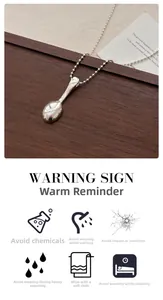 Detailed view of silver spoon pendant necklace on black cord with care instructions