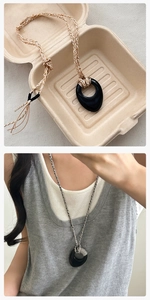 Dettaglio di una collana lunga minimalista con pendente ovale nero e catena in corda intrecciata