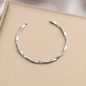Silver twisted spiral stainless steel bangle with polished finish on a display stand