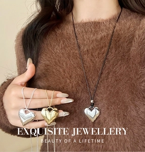 Detail van een 3D metalen hartvormige hanger aan een lange ketting op een trui
