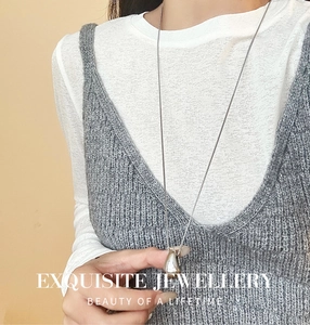 Polished silver teardrop pendant necklace worn over a gray knitted vest for women