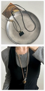 Dettaglio del ciondolo a cuore in occhio di tigre e mini borsa nera su collana lunga intrecciata