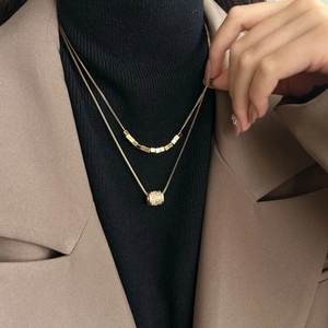 Dubbellaagse gouden titanium ketting met kubuskralen en kristallen cilinder hanger op model
