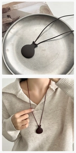 Dettaglio della collana con ciondolo a forma di bollitore scuro su un maglione bianco