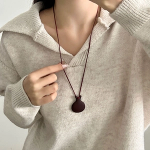 Ciondolo a teiera minimalista rosso scuro su cordino in pelle con maglione beige
