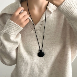 Collana con ciondolo a sacchetto nero opaco su un maglione beige lavorato a maglia