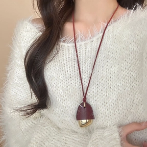Minimalistische Eichel-Halskette aus rotem Leder und mattem Gold auf weißem Pullover