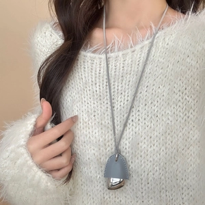 Lange silberne Halskette mit grauem Lederdetail auf weißem Strickpullover