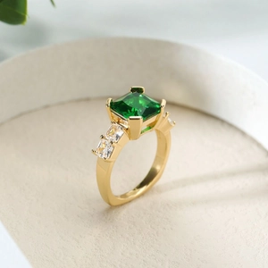 Elegante goudkleurige ring met een vierkant geslepen groene steen en zij-accenten