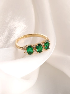 Détail macro de bague en argent S925 doré avec trois pierres ovales vert émeraude sur soie