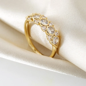 Eleganter vergoldeter Wellenring mit runden und marquise Zirkonia auf beigem Seidengrund