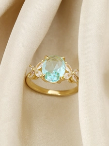 Macro di anello dorato con zircone blu ovale e dettagli floreali su seta elegante