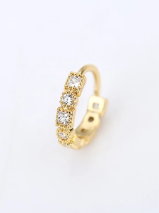 Dettaglio macro di orecchino huggie dorato con zirconi brillanti incastonati