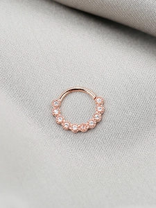 Dettaglio macro di un anello al naso in oro rosa con 10 zirconi scintillanti su seta grigia
