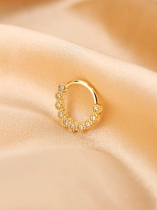 Dettaglio di un anello al naso dorato con zirconi bianchi su sfondo di seta champagne