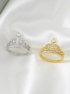 Detailed view of silver and gold crown rings with zircon stones on white silk fabric