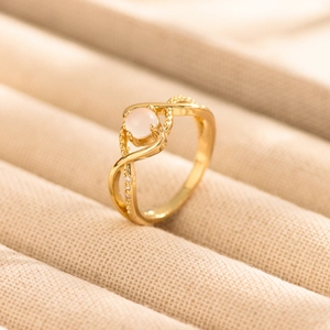 Elegant gold crossover ring with pink round gemstone and white accents on beige velvet