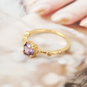 Macro shot of a square purple gemstone ring with gold band and white side accents