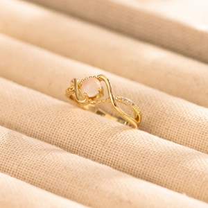 Detailed close-up of a golden wave ring featuring a pink stone and small diamond accents