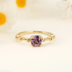 Close-up of elegant gold ring featuring square purple crystal and small side diamonds