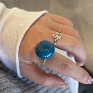 Détail d'une bague en résine bleue et d'un anneau argenté avec une croix gothique au doigt