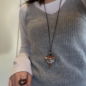 Detail of ebony wood heart pendant wrapped in silver metal wires on a knitted vest