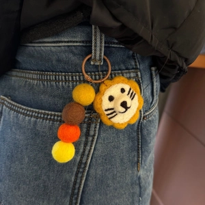 Handmade lion felt charm with colorful wool beads shown attached to denim jeans loop