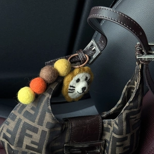 Detail of handmade wool felt charm with cute lion and gradient beads on a canvas bag