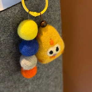 Close-up of handmade yellow felt chick phone charm with colorful beads and fluffy texture
