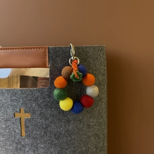 Detail of colorful handmade felt bead charm hanging on a grey bag with a silver metal clasp