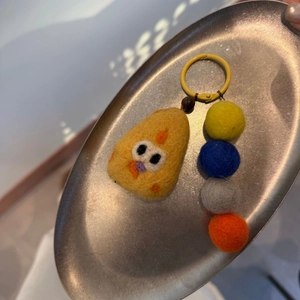 Detail of handmade yellow wool felt chick charm with colorful beads on a metal tray