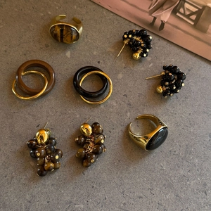 Platliggende vintage tijgeroog en obsidiaan ringen en kralen oorbellen op steen