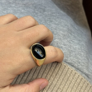 Gepolijste gouden zegelring met ovale zwarte obsidiaansteen gedragen aan vinger voor details