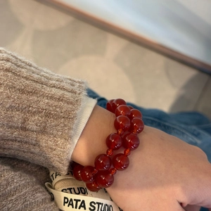 Detail of a double-strand red agate beaded bracelet worn on a wrist with brown knitwear