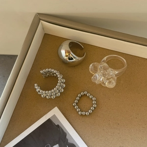 Flache Ansicht von silbernen Ohrmanschetten und transparentem Blumenharzring