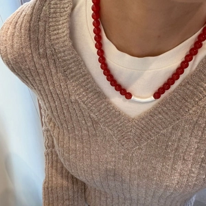 Close-up of red agate beaded necklace with white curved tube accessory worn by model