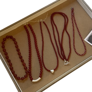 Red agate bead necklaces with silver heart and bar pendants on beige jewelry tray