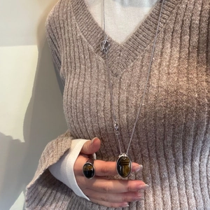 Set collana lunga con ciondolo occhio di tigre e anello su sfondo maglione marrone