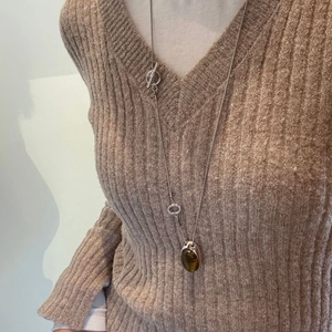 Dettaglio di una lunga collana d'argento con ciondolo occhio di tigre su maglione marrone