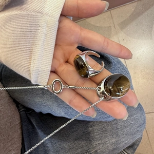 Dettaglio della collana con occhio di tigre marrone e anello aperto abbinato sulla mano
