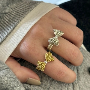 Detailed view of handmade beaded bow rings in silver and gold with pearl accents