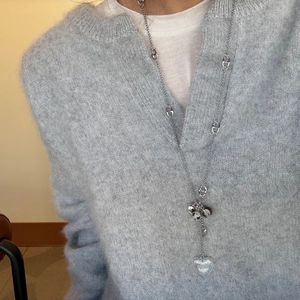 Détail d'un long collier argenté avec pendentif coeur sur un pull en mohair bleu